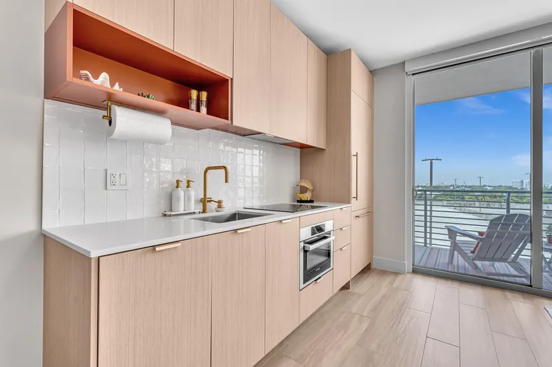 Kitchen with light oak cabinets, white tile and a gold faucet